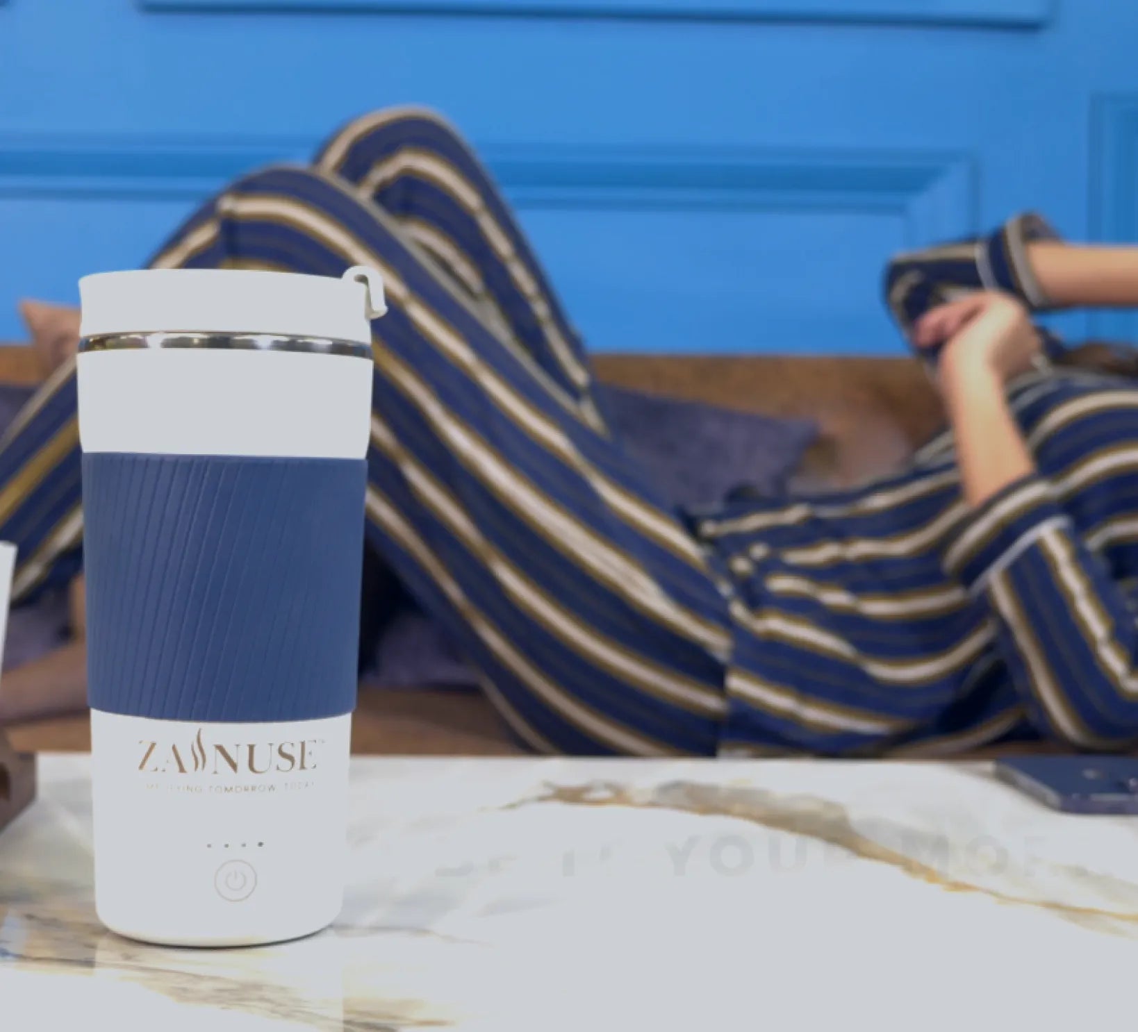 Blue and white tumbler with 'ZANUSE' branding on a marble surface, person sitting in striped pants in the background.