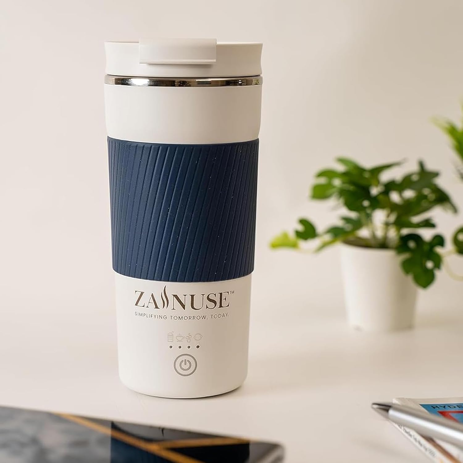 White and blue travel mug with 'Zainuse' branding on a desk with a plant in the background.